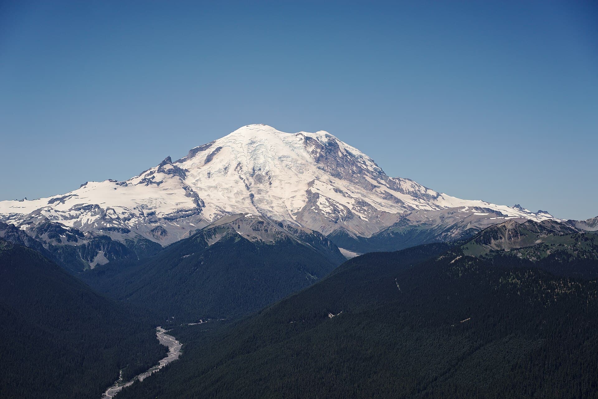 Mount Rainier as viewed in the summer from Silver Queen Peak , near Crystal Mountain resort at an elevation of around 7000 ft looking west by southwest. The main summit, Columbia Crest (14410 feet) is at the center. The White River is visible in the lower left.